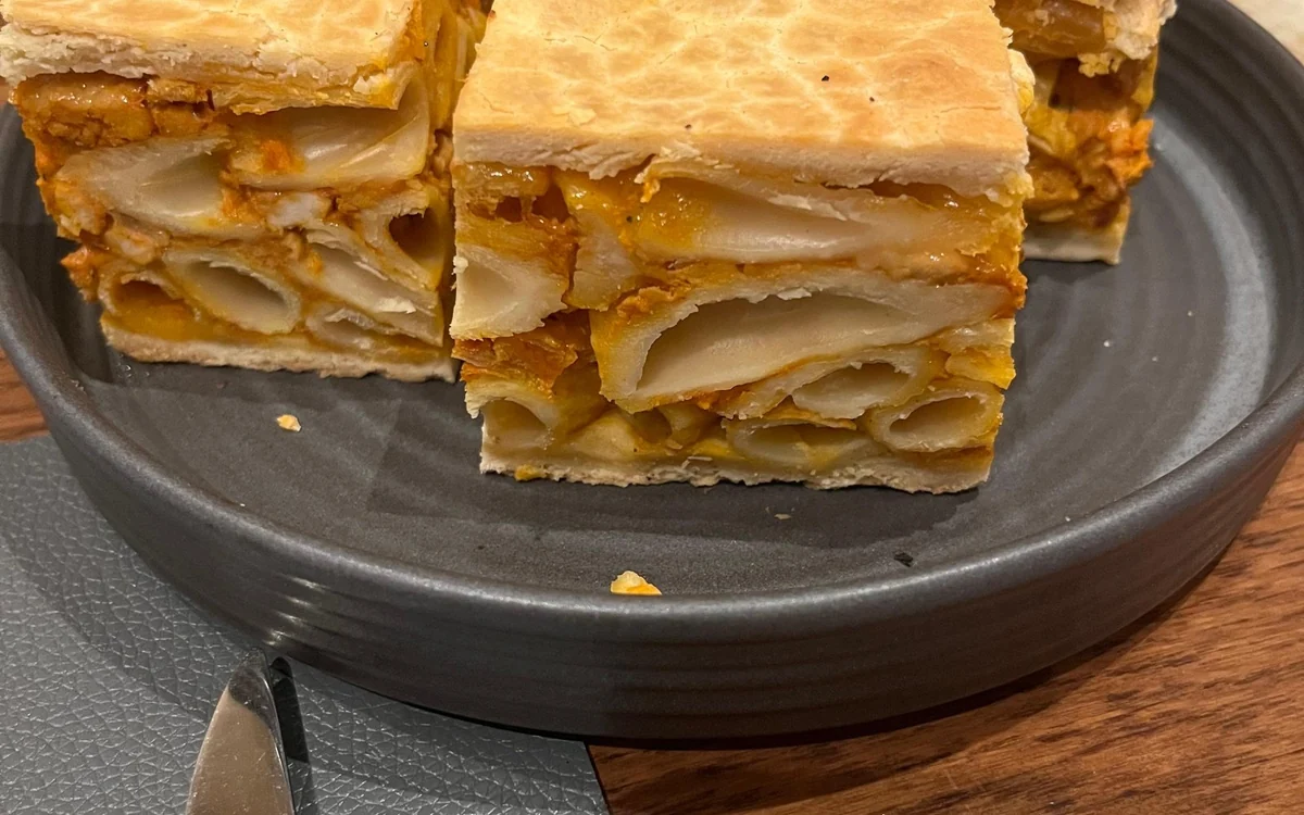 Cuadrados de pasta al horno bajo una tapa de hojaldre en un plato oscuro
