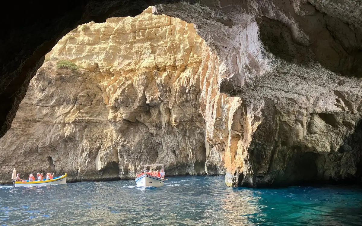 Two small boats with passengers in orange life jackets inside a sea cave, turquoise water