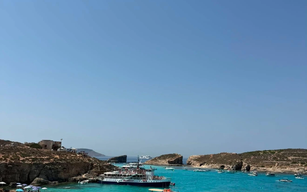 Tour boats moored in turquoise water off Comino, with sun umbrellas on the rocks
