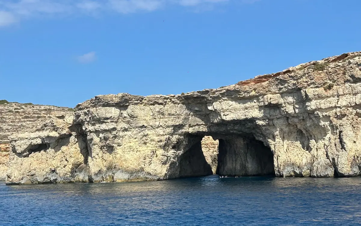 A sea cave opening at the waterline of pale limestone cliffs above deep blue water