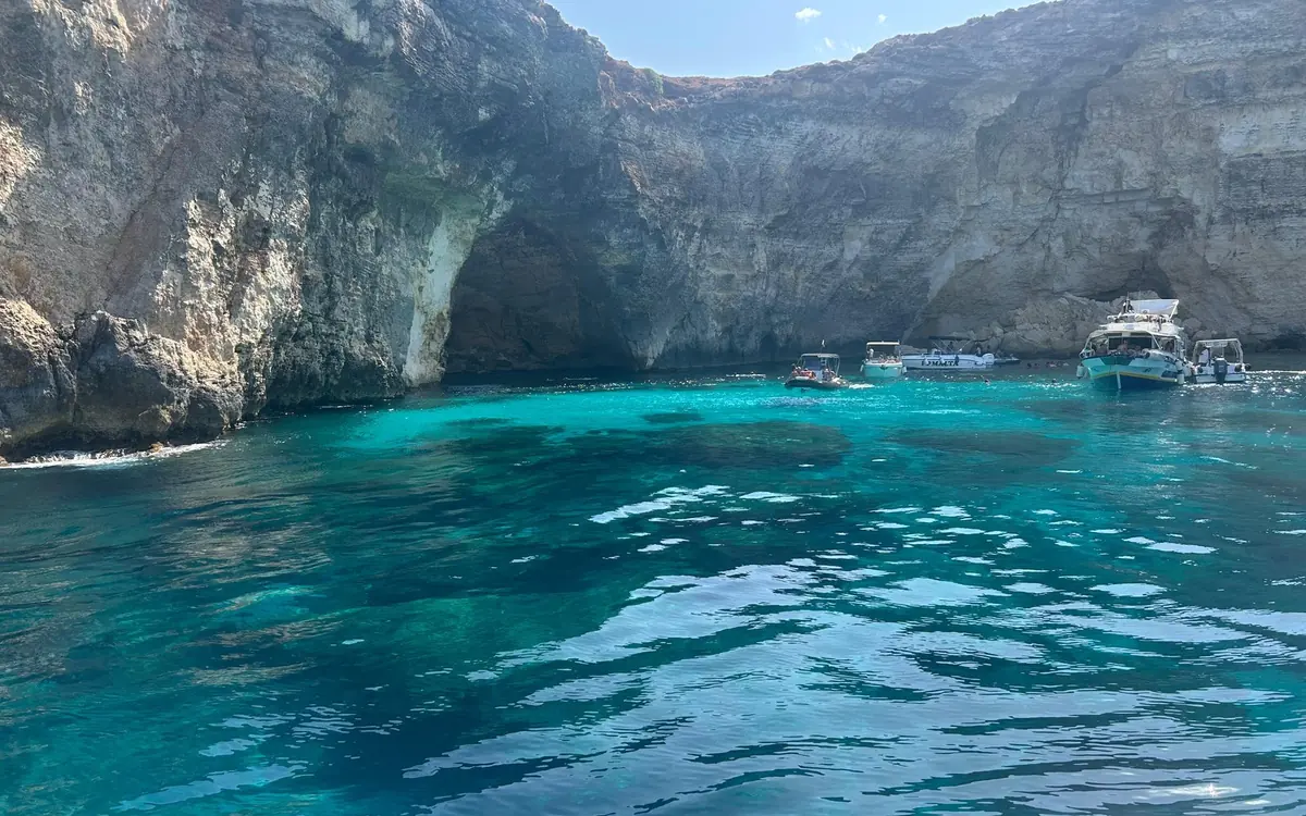 Eine Bucht mit leuchtend blauem Wasser unter hellen Klippen, kleine Boote nahe einer Höhle