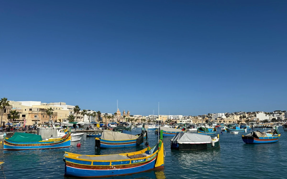 Brightly painted fishing boats moored in the harbour at Marsaxlokk, church towers beyond