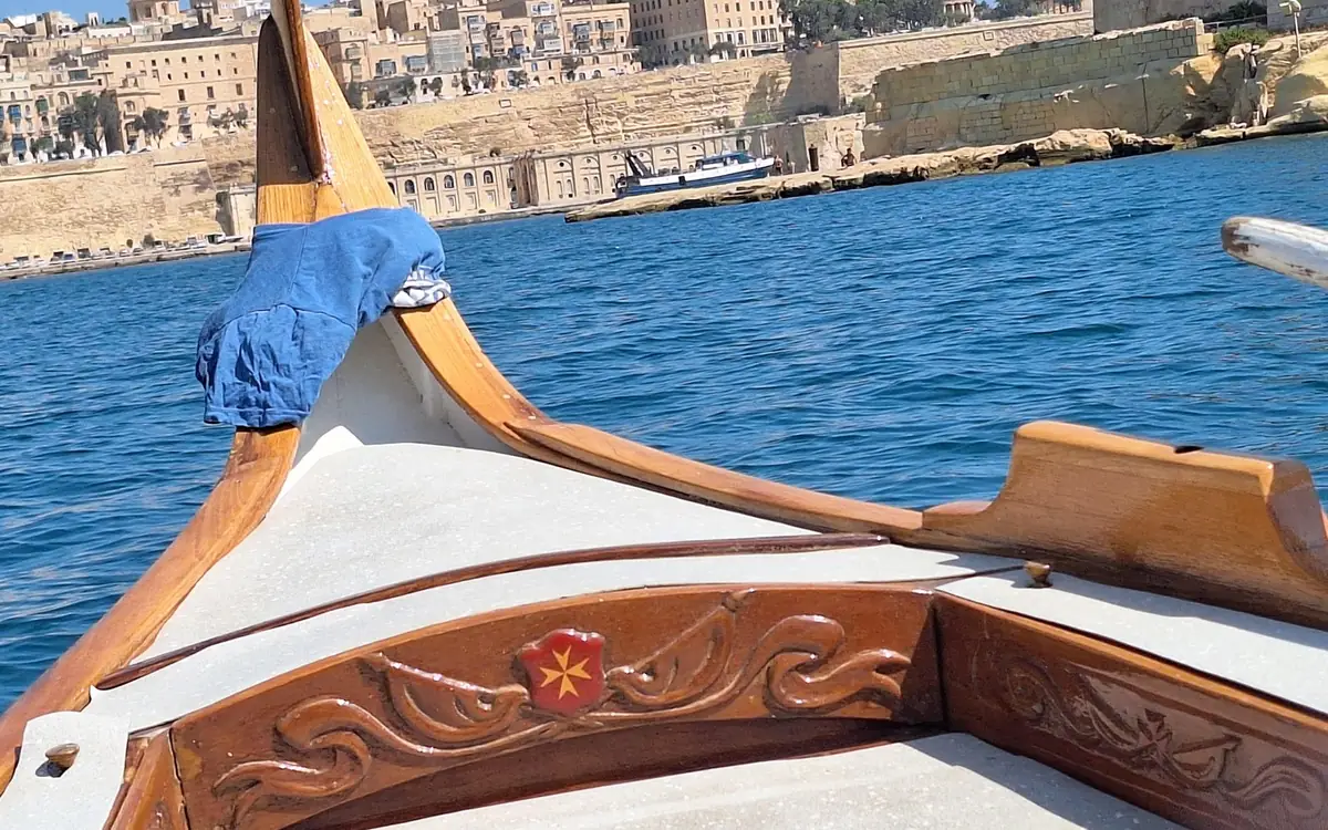 The carved wooden bow of a traditional boat on the harbour, a fortified waterfront beyond
