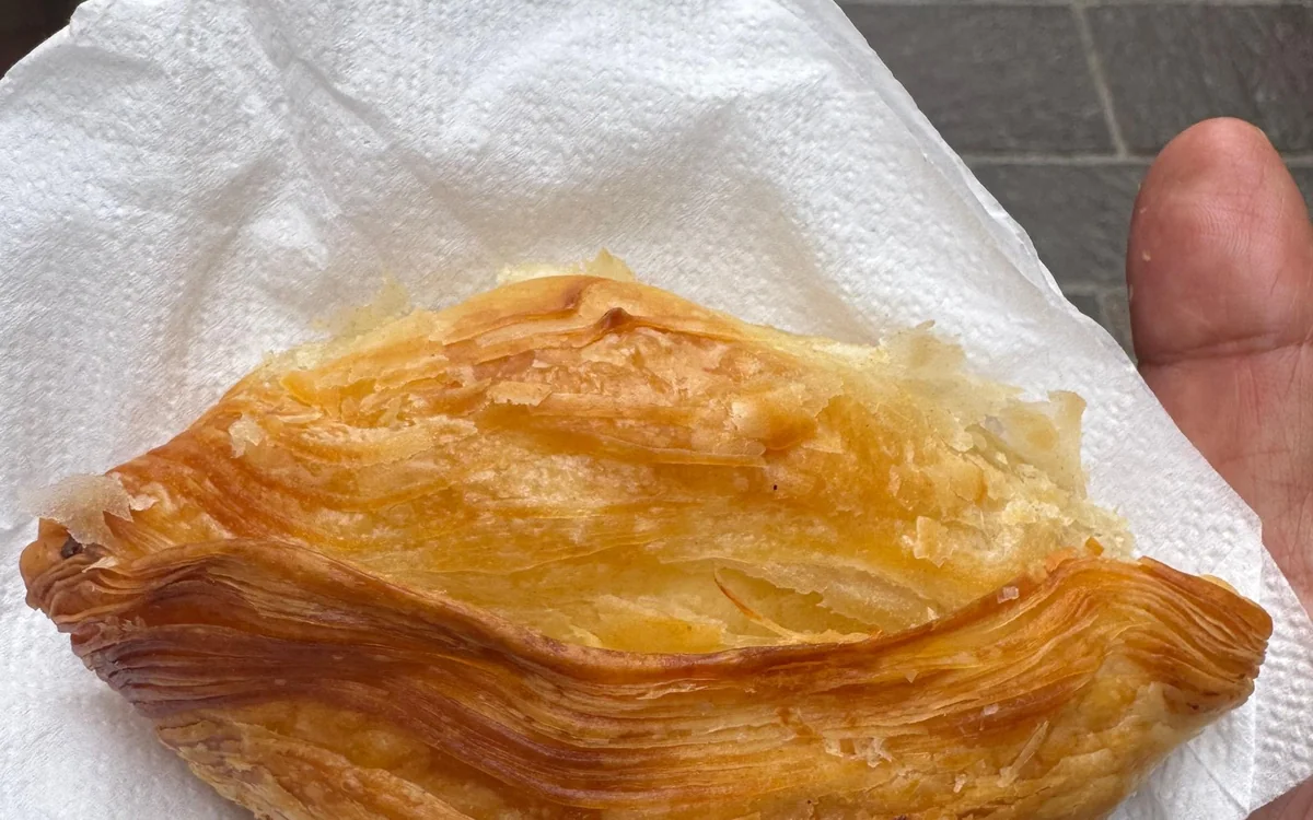 A flaky golden pastizz on a paper napkin, held in one hand