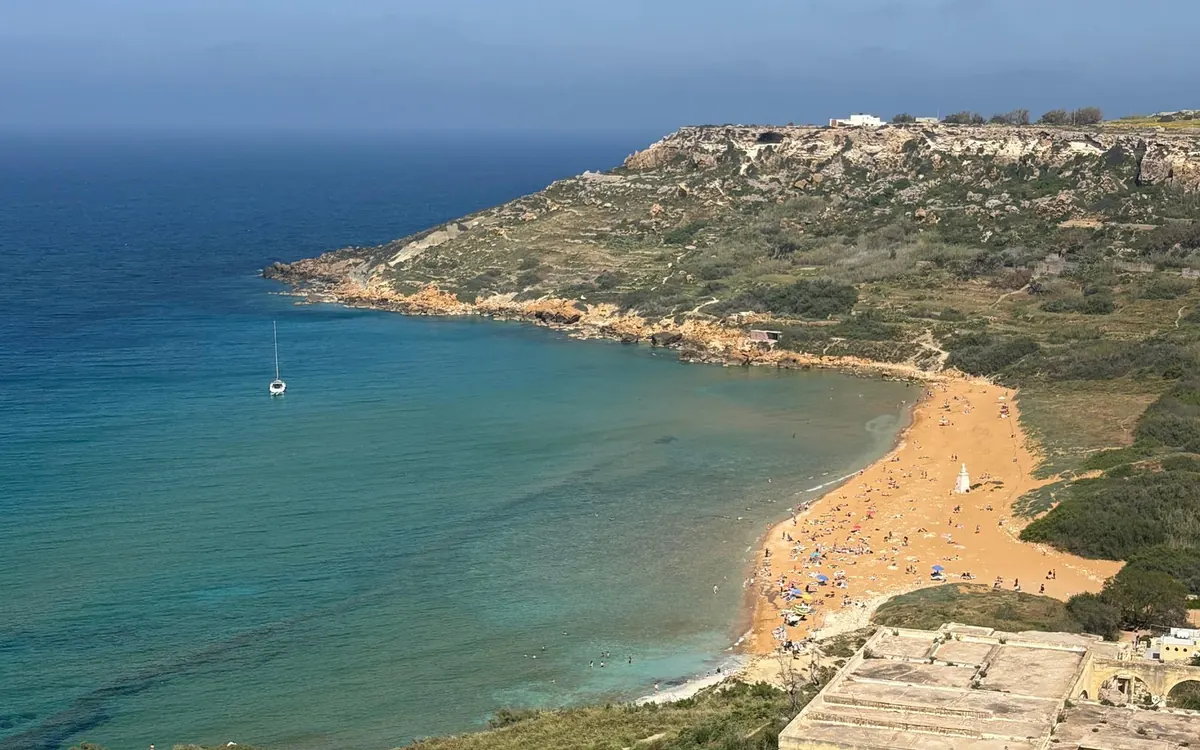The red sand of Ramla Bay on Gozo from the hill above, a sailing boat at anchor offshore