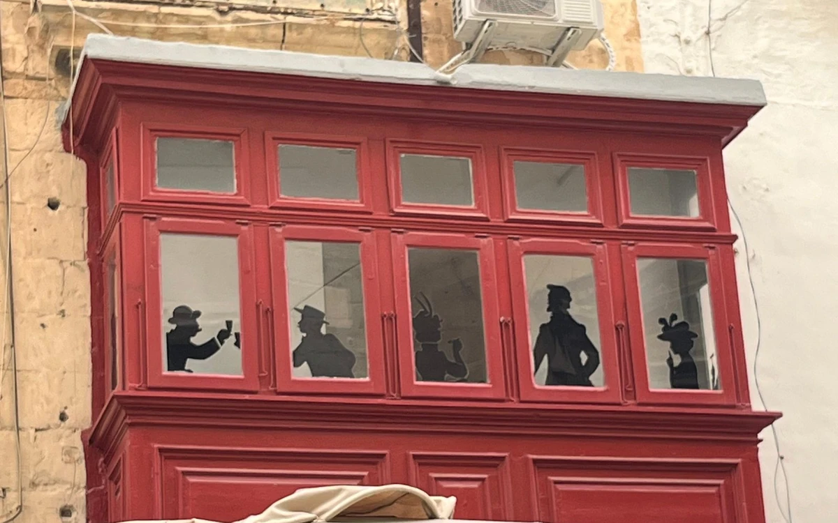 Un balcón de madera rojo cerrado con siluetas pintadas en sus ventanas