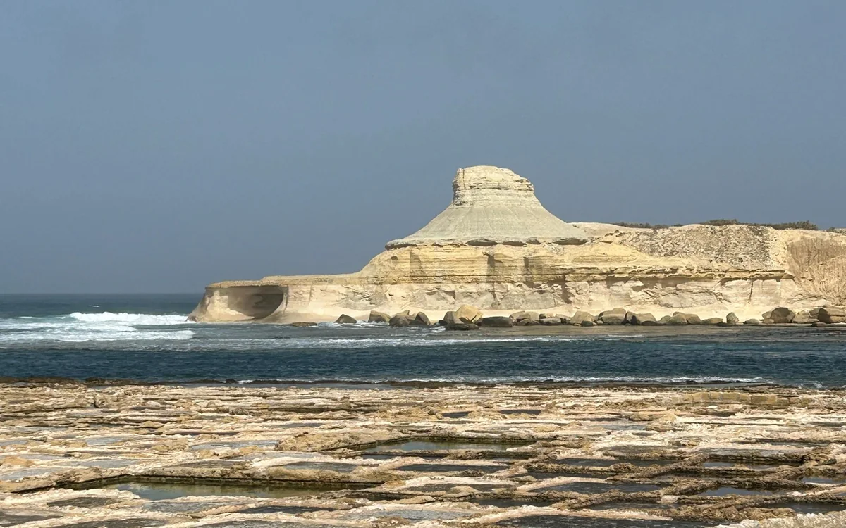 Salt pans cut into the rock on the Gozo coast, a pale sandstone headland beyond