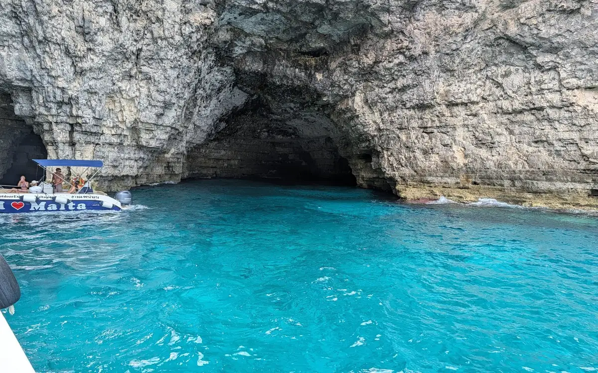 Ein kleines offenes Boot mit Passagieren am Eingang einer Meereshöhle in hellen Klippen