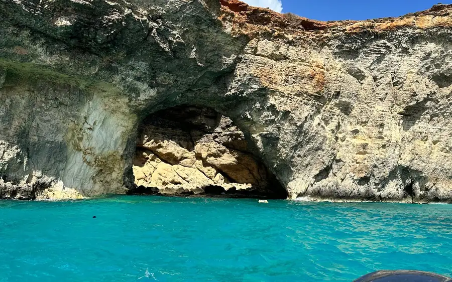 Eine Höhle in geschichteten Klippen über türkisfarbenem Wasser, vom Boot aus gesehen