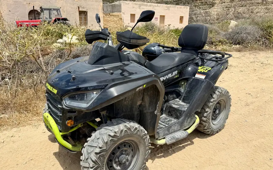 Ein schwarzes Quad auf einem Sandweg neben einem Bauernhaus