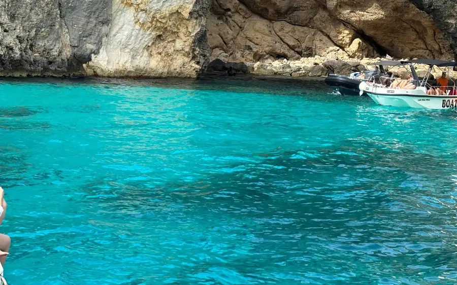 Ein kleines Motorboot in leuchtend türkisfarbenem Wasser unter Klippen und einer Meereshöhle