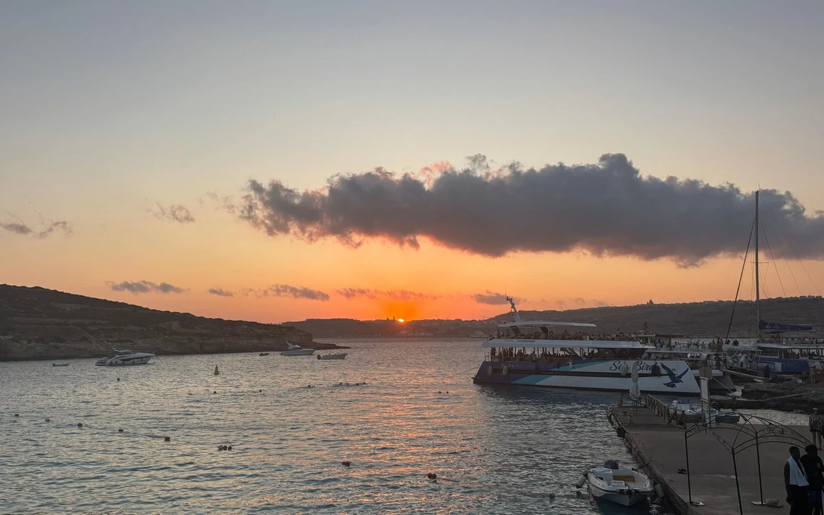 The sun dropping behind the hills over a bay, a large excursion boat tied up at the jetty