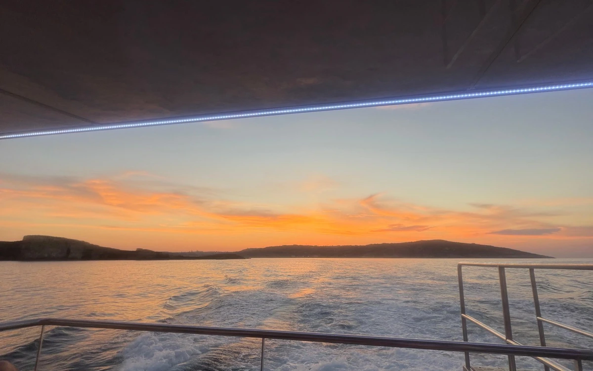 An orange sky over low headlands, seen from under the canopy at the stern of a boat
