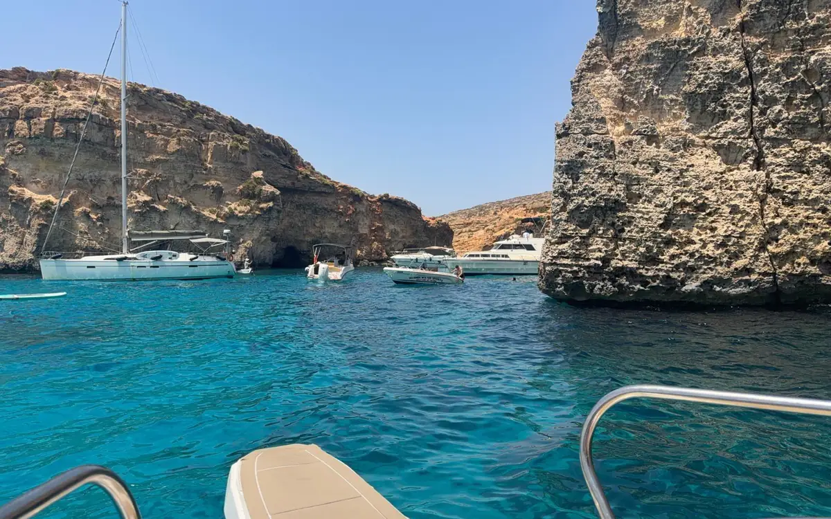 Eine Segelyacht und Motorboote in einer schmalen Bucht zwischen felsigen Klippen, vom Bug aus gesehen